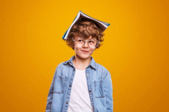 Garçon rieur à lunettes, un livre posé sur la tête
