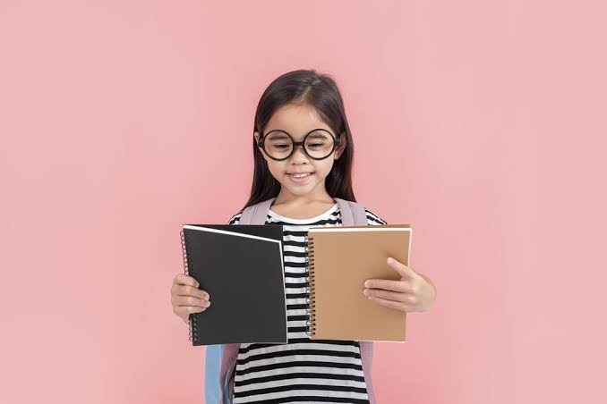 Fillette à grandes lunettes rondes, un cahier dans chaque main