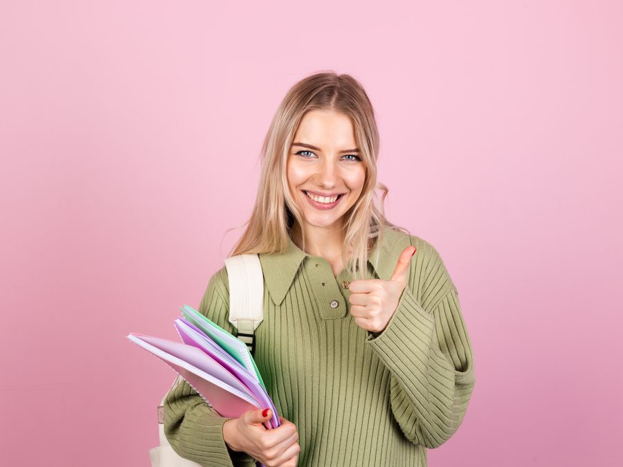 Jeune femme souriante tenant des cahiers colorés, pouce levé