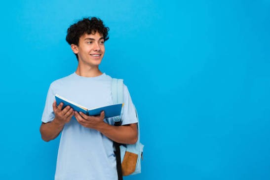 Lycéen souriant, un livre ouvert à la main, sac à dos sur l’épaule